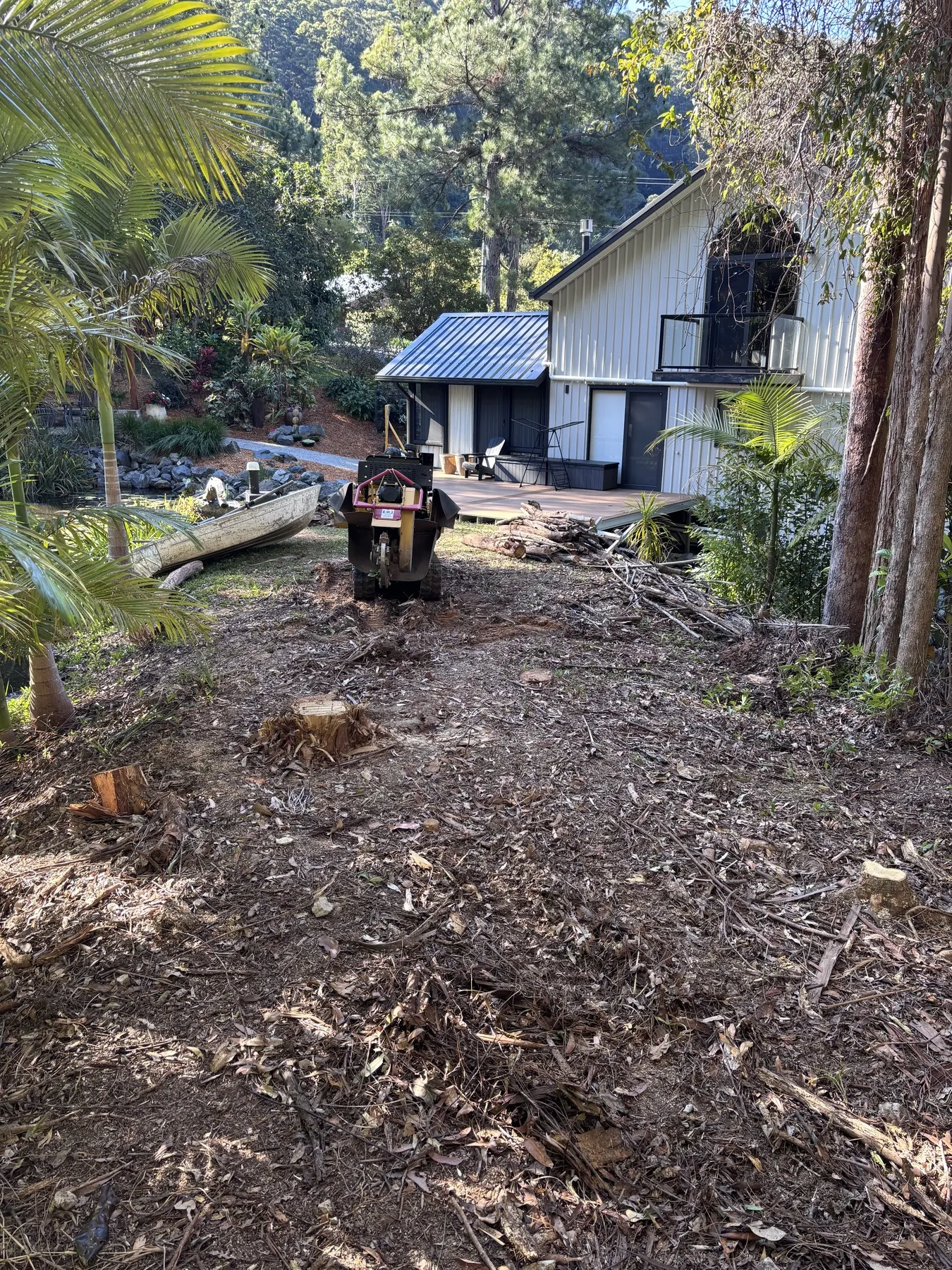 Stump grinder clearing a mulch-covered slope beside a home